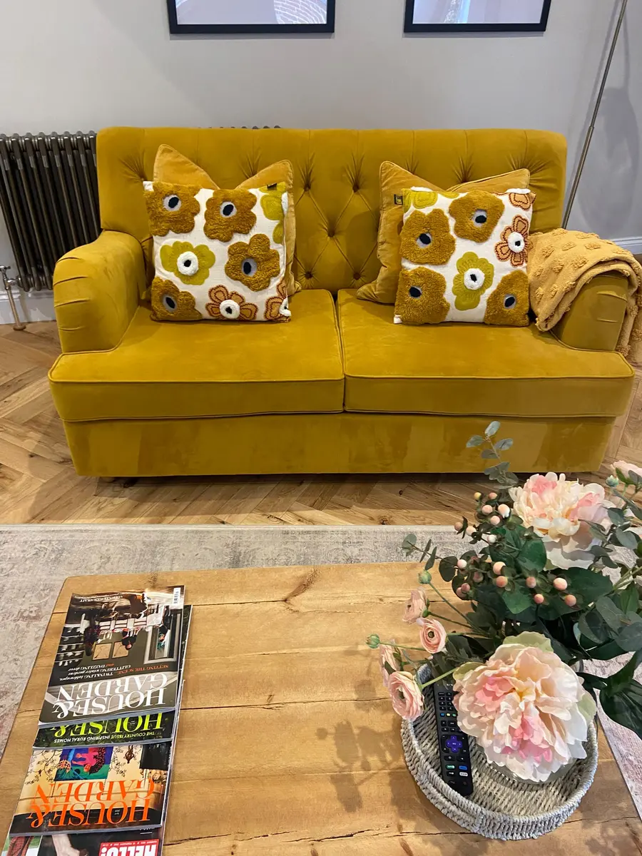 Mustard velvet sofa with cushions and fresh flowers on the coffee table